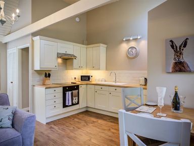 A kitchen with white cabinets wooden countertops a dining table with chairs and a rabbit painting on the wall at Lime Tree in Burford