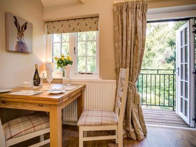 A dining area with a wooden table and two chairs near a window and open door to a balcony at Lime Tree in Burford
