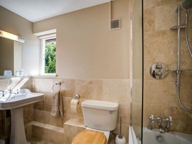 A bathroom with a pedestal sink toilet with wooden seat bathtub with shower at Lime Tree in Burford