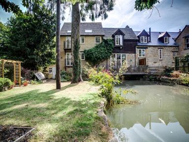 A garden with grass trees and a pond in front of a stone house with balconies at Lime Tree in Burford