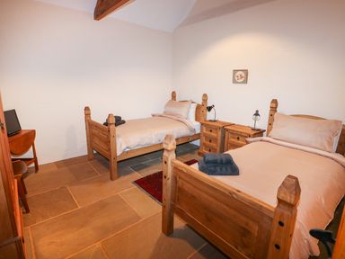A bedroom with two wooden single beds bedside tables and a small television at Honey Buzzard Barn in Fakenham