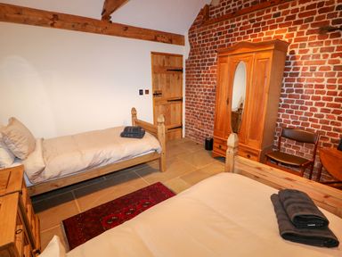 A bedroom with two single beds a wooden wardrobe a chair a small rug and exposed brick wall at Honey Buzzard Barn in Fakenham