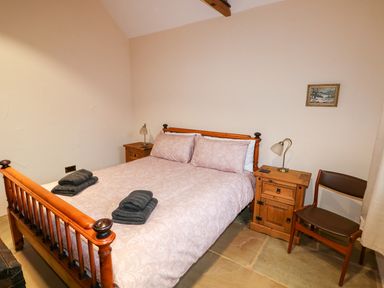 A bedroom with a wooden bed and side tables with lamps and a chair at Honey Buzzard Barn in Fakenham