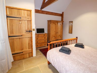 A bedroom with a wooden bed frame chest of drawers wardrobe and a wooden door at Honey Buzzard Barn in Fakenham