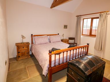 A bedroom with a wooden bed and nightstands next to a curtained window at Honey Buzzard Barn in Fakenham