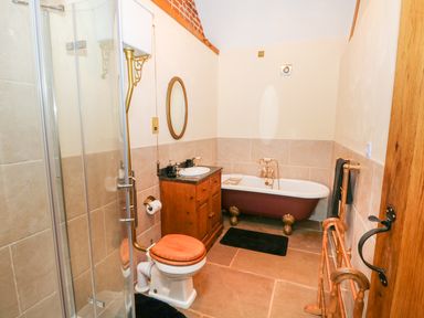 A bathroom with a glass shower enclosure wooden toilet seat wooden cabinet sink clawfoot bathtub and towel rail at Honey Buzzard Barn in Fakenham