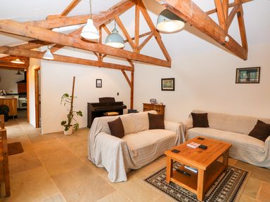 A living room with exposed wooden beams two sofas covered with fabric a wooden coffee table and a piano at Honey Buzzard Barn in Fakenham