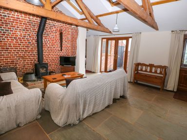 A living room with two covered sofas wooden coffee table wood stove under exposed beams at Honey Buzzard Barn in Fakenham