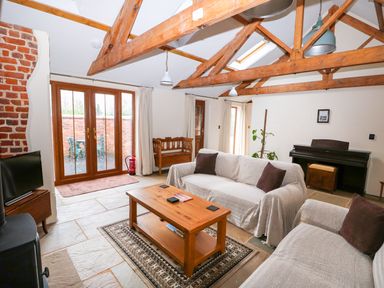 A living room with wooden beams two sofas a wooden coffee table a piano and a TV at Honey Buzzard Barn in Fakenham