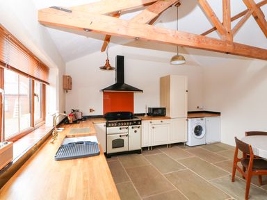 A kitchen with wooden beams wooden countertops a stove a washing machine a microwave and a dining table at Honey Buzzard Barn in Fakenham
