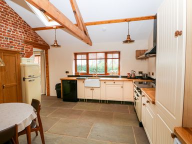 A kitchen with wooden beams a round table cream cabinets and a window at Honey Buzzard Barn in Fakenham