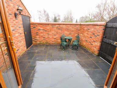 A small outdoor patio with black tiled floor green metal table and three chairs enclosed by red brick walls at Honey Buzzard Barn in Fakenham