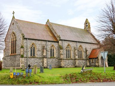 A stone church building with arched windows and a bell tower on a grassy area near Croxton Road