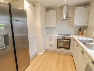 A kitchen with stainless steel fridge oven stove white cabinets and wooden floor at Ty Taid in Rhosneigr