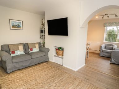 A living room with a grey sofa a wall-mounted television and an adjacent room with grey armchairs at Ty Taid in Rhosneigr