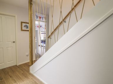 A staircase with rope railings next to a door and a hallway leading to a room with bunk beds and bunting at Ty Taid in Rhosneigr