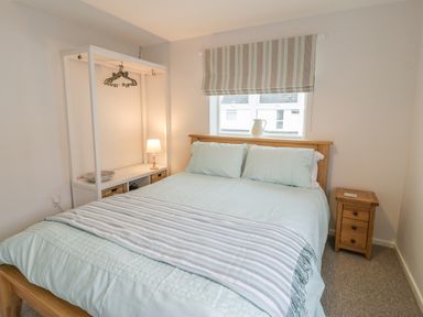 A bedroom with a wooden bed frame and light blue bedding next to a window with striped blinds and a wooden nightstand at Ty Taid in Rhosneigr
