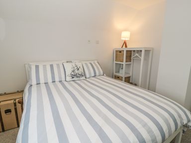 A bedroom with a double bed with striped bedding a storage unit with baskets and a lamp at Ty Taid in Rhosneigr