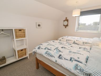 A bedroom with two single beds a window a wall mirror and a white shelving unit with baskets at Ty Taid in Rhosneigr