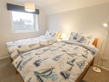 A bedroom with two single beds with sailboat patterned bedding a window and two lamps at Ty Taid in Rhosneigr