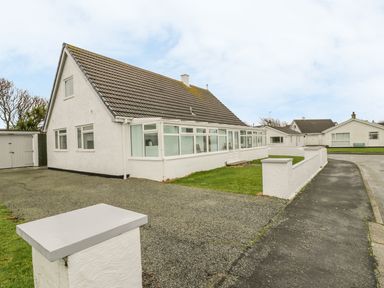 A white house with a tiled roof and a long enclosed porch with windows along the front at Ty Taid in Rhosneigr