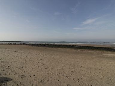 A sandy beach with scattered rocks and footprints with sea and sky in the background at Ty Taid in Rhosneigr