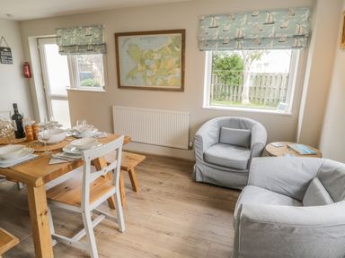 A dining area with a wooden table set for four and two gray armchairs near a window at Ty Taid in Rhosneigr