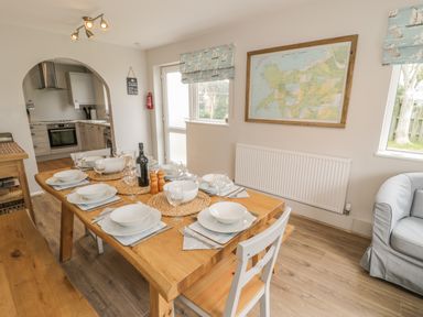 A dining area with a wooden table set with dishes and glassware next to a kitchen and a seating area at Ty Taid in Rhosneigr