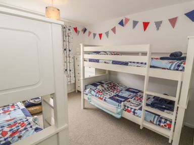 A bedroom with two white bunk beds with nautical bedding and a chest of drawers at Ty Taid in Rhosneigr