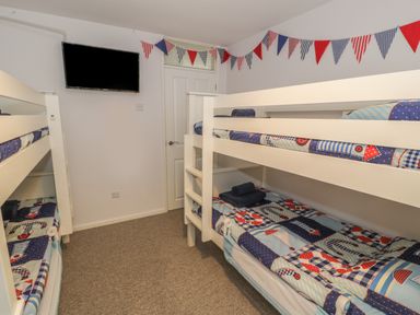 A bedroom with two white bunk beds a wall-mounted television and bunting decoration at Ty Taid in Rhosneigr