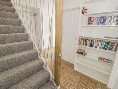 A carpeted staircase next to a bookshelf with books and dvds in a hallway with two white doors at Ty Taid in Rhosneigr