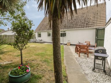 A backyard with a small tree and flowers in a pot patio furniture and a barbecue grill at Ty Taid in Rhosneigr