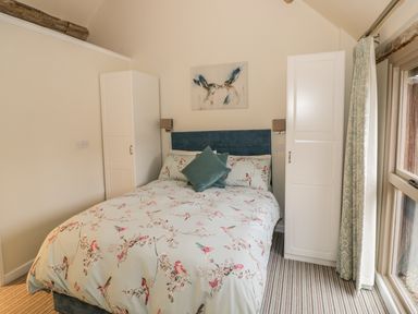 A bedroom with a bed between two white wardrobes and a window with curtains at Megs Cottage in Tiddington