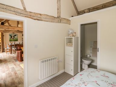 A bedroom with a striped carpet and bird patterned bedding with visible bathroom and dining area at Megs Cottage in Tiddington