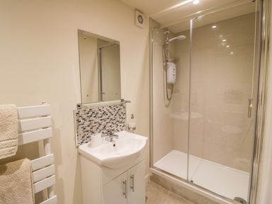 A bathroom with a shower enclosure a white sink with cabinet and a towel rack with beige towels at Megs Cottage in Tiddington