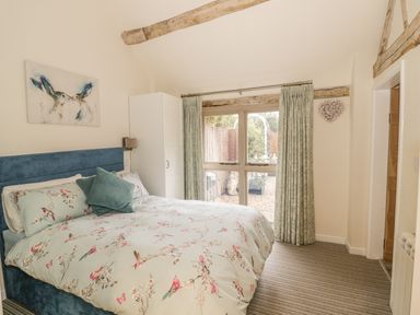 A bedroom with bed floral bedding wardrobe and window with curtains at Megs Cottage in Tiddington