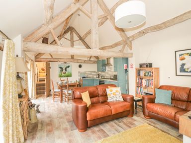 A living room and kitchen area with exposed wooden beams two brown leather sofas and a dining table at Megs Cottage in Tiddington