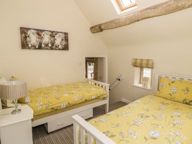 A bedroom with two single beds with yellow floral bedding and a bedside table with a lamp at Megs Cottage in Tiddington