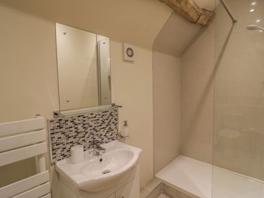 A bathroom with a sink and mirror above a tiled backsplash and a walk-in shower at Megs Cottage in Tiddington