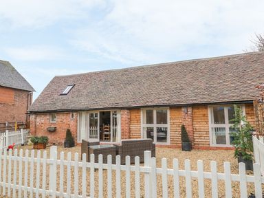 A single story house with brick and wood exterior a gravel yard outdoor furniture and a white picket fence at Megs Cottage in Tiddington