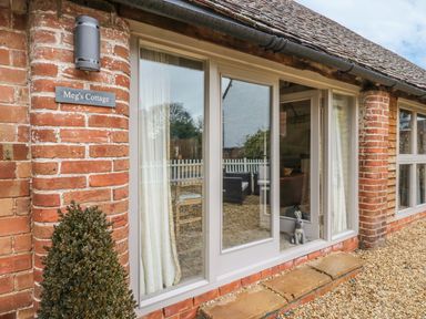Exterior view of a brick cottage with large windows a small bush and a nameplate reading Megs Cottage at Megs Cottage in Tiddington