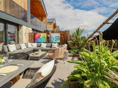 An outdoor patio with a sectional sofa dining table chairs plants and modern artwork at Stargazers in Sennen