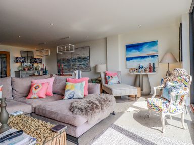 A living room with a gray sectional sofa with colorful pillows a patterned armchair a chaise lounge and artwork on the walls at Stargazers in Sennen