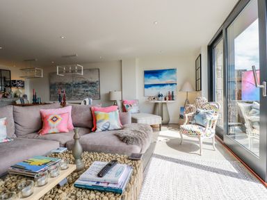 A living room with a sectional sofa and colorful cushions beside glass doors at Stargazers in Sennen