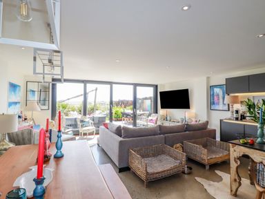 A living room with a gray sofa two wicker baskets a wooden table and large glass doors at Stargazers in Sennen