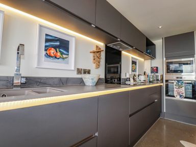A kitchen with gray cabinets and integrated appliances and under-cabinet lighting at Stargazers in Sennen