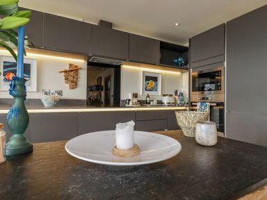A kitchen with dark cabinets a built in oven and microwave a countertop with candle holders and a plate with a candle at Stargazers in Sennen