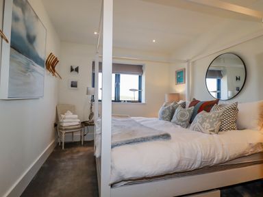 A bedroom with a four poster bed pillows a chair with towels a round mirror and wall art at Stargazers in Sennen