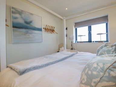 A bedroom with a bed pillows a painting window with fish decorations and a lamp at Stargazers in Sennen