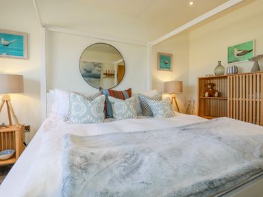 A bedroom with a large bed and decorative pillows bedside tables with lamps a mirror and wooden shelving at Stargazers in Sennen